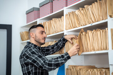 Young office worker searching files in archive room, organizing documents on shelves, storing information