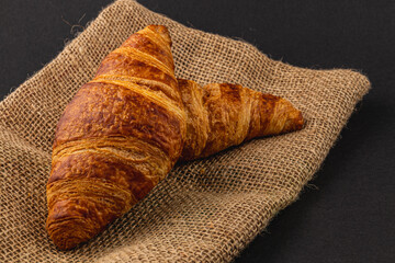 Fresh golden croissants on burlap on black background, for breakfast