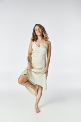 Beautiful young woman with vitiligo poses gracefully in a light dress against a neutral backdrop.