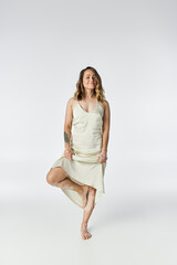 Young woman shows her unique beauty while standing elegantly on one leg in a light dress.