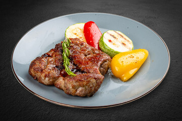 Grilled pork steak served with a colorful assortment of charred vegetables.