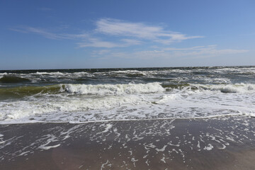 Gentle Waves on a Sunny Beach: A scenic view of ocean waves gently reaching the sandy shore under a clear blue sky, capturing the tranquility and beauty of coastal nature.