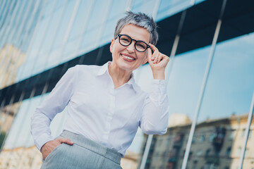 Confident mature businesswoman with grey hair and glasses standing outdoors in urban setting