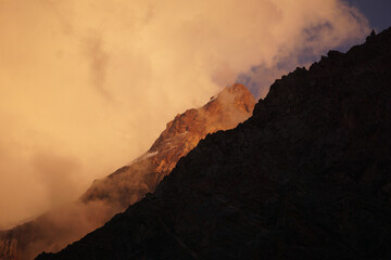 Fototapeta premium Mountain rock peaks are shrouded in clouds during sunset