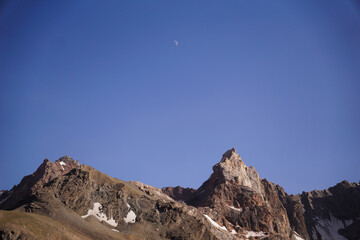 The moon appears over mountain peaks and cliffs. Mountain landscape during sunset
