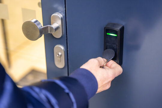 Close up view of person using a electric lock key fob to access a building via a reader of entry system mounted on a house wall