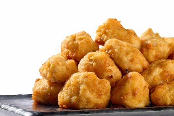Close-up of crispy golden chicken nuggets piled on a black plate against a white background.