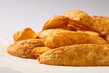 Golden and crispy potato wedges served on white paper.