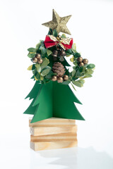 Closeup view of a Christmas tree miniature on a pile of wooden blocks with a star and Christmas wreath on a white background