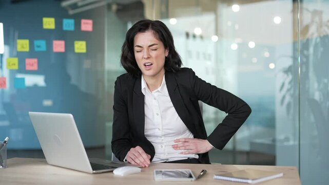 Businesswoman sitting in office. holding stomach, indicating stomach pain or abdominal discomfort. Sick worker has heartburn, gastritis or poisoning. Female suffers from spasms and is constipated