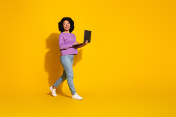 Full length photo of pretty young woman laptop walk empty space isolated on yellow color background