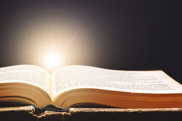 Fototapeta premium An open book with light shining from it. Black book glares at the background. Book opens up with a glare of black sun glare. A book opens up with a glare of black and white against lifestyle a dark.