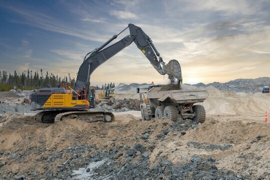 An excavator loads a dump truck with soil at sunset on a construction site
