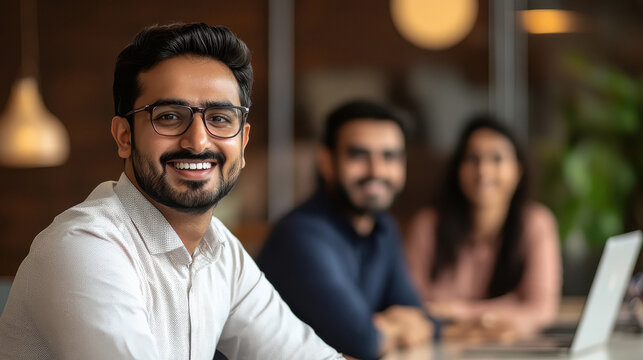 Indian employee sitting in his desk smiling stress free with his colleague and his manager in a corporate office