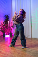 Fototapeta premium A young woman dances in a studio, her hair pulled back in a ponytail, with a pink and blue light illuminating the space