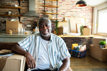 Portrait of a happy senior black man in apartment filled with moving boxes