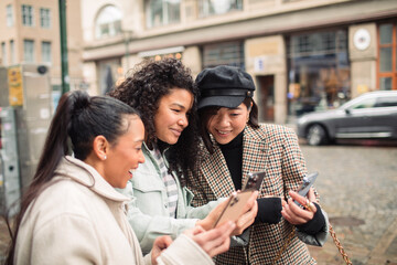 Young stylish female friends pointing while using phone for directions in the city