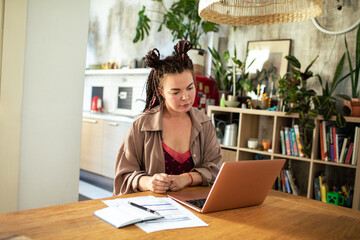 Woman focused on work on laptop in home office with plant decor