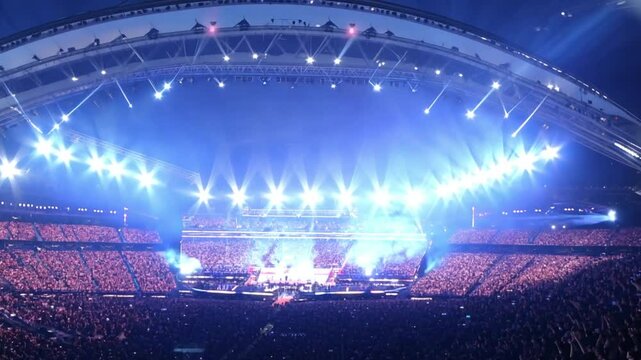 A massive stadium brightly lit at night, hosting a sports event or concert with thousands of excited spectators in the stands.