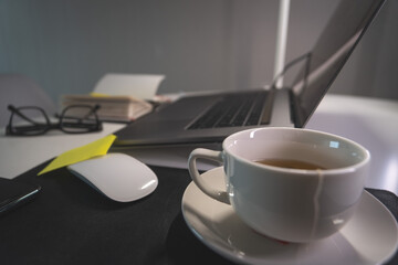 A white coffee cup sits on a table next to a laptop