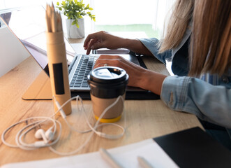 A woman is typing on a laptop while holding a cup of coffee. remote work concept