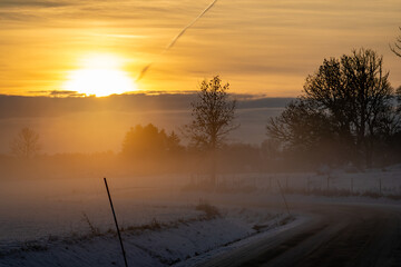 Fototapeta premium Uppsala, Sweden The sun sets over a rural road in a frosty and misty landscape.