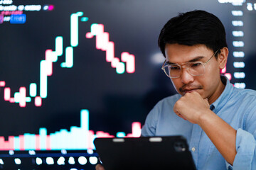 A man is looking at a computer screen with a graph on it. He is wearing glasses and he is deep in...