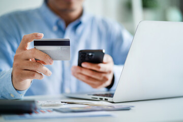 A man is holding a credit card and a cell phone, possibly using them to make a purchase