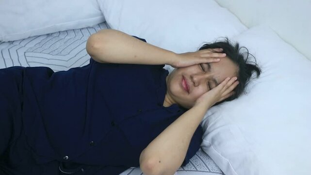 Sleepy women lying on bed massaging forehead suffering headache. Healthcare concept