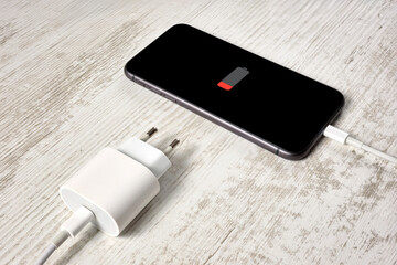 A modern smartphone with a low battery level lies on a beautiful vintage table. The device is...