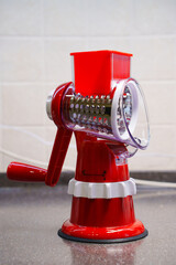 a red mechanical grater on the kitchen table. Multislicer grater for vegetables and fruits 3 in 1...