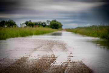 Selective focus on the gravel leading into floodwater covering the road in a rural area