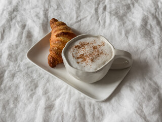 Cappuccino with cinnamon and fresh crispy croissant - lazy morning, breakfast in bed