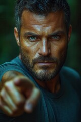 Fototapeta premium Man with intense expression points aggressively while surrounded by dark forest environment in a close-up shot during daylight