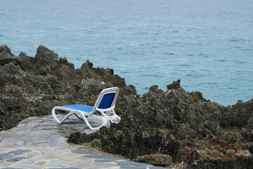 Secluded lounger by the rocky shoreline overlooking a tranquil ocean landscape during a rainy day.