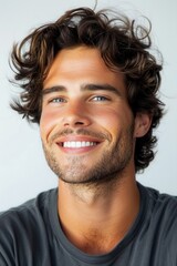 Obraz premium Smiling young man with curly hair poses casually against a light background showcasing his bright, cheerful demeanor during a relaxed moment