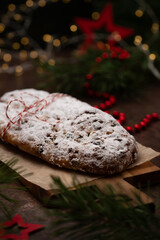 German Christmas stollen cake on a wooden cutting board on a rustic background with lights and decorations. Traditional handmade Christmas dessert. Fruit bread with nuts, raisins and marzipan.