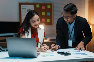 Two asian businesspeople are working late in their office, taking notes and smiling during a meeting