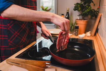 Mann brät sich ein Stück Fleisch zu Hause in der Pfanne