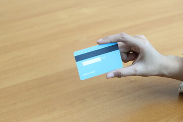 A Person Holding a Light Blue Credit Card Above a Wooden Table: Online Shopping, Banking, and Finance Concept