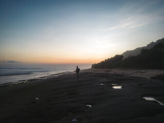 A lone figure walks along the tranquil beach at dawn.