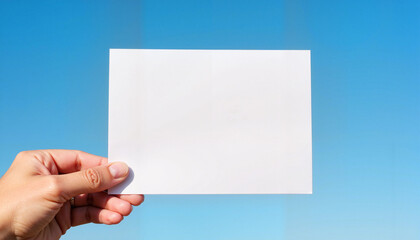 Obraz premium Person holding blank white paper against clear blue sky 
