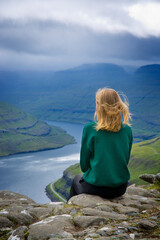 Unrecognizable girl sitting by the Funningfjordur in the Faroe Islands. View from vantage point...