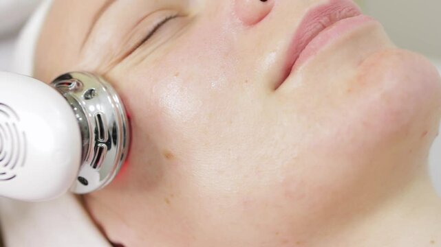 Beautician performing a cosmetic procedure on a woman's face with a specialized radiofrequency lifting device. Beauty Clinic Concept