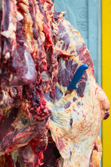 Obraz premium A knife is stabbing in a big piece of raw beef or yak meat that hang at the butchery shop. Food object photo, selective focus.