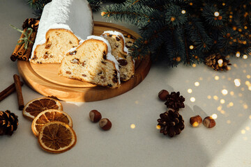 Christmas stollen on a wooden board with green branches of a Christmas tree on light grey background. Christmas background, Christmas desserts