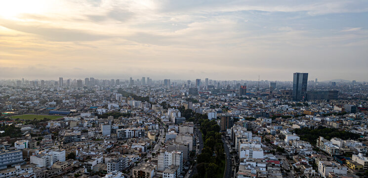 Aerial photography capturing the vibrant and bustling San Borja district of Lima, Peru, on a warm orange summer afternoon, featuring a prominent building in the distance