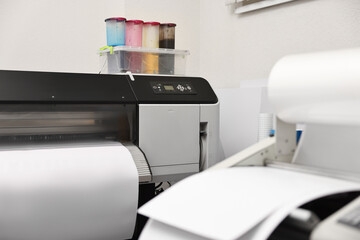 Wide-format printer and roll laminator with paper indoors, selective focus. Printing house