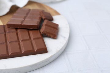 Pieces of delicious milk chocolate on white tiled table, closeup. Space for text