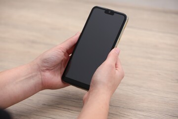 Woman holding smartphone with blank screen at wooden table, closeup